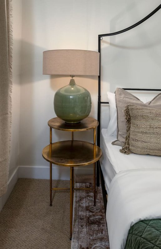 Bedroom corner with round side table, green ceramic lamp base, linen shade, and white bedding