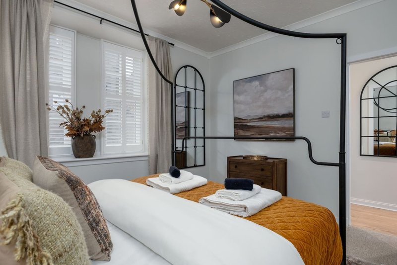 Modern bedroom with metal four-poster bed, white bedding, wooden nightstands and landscape artwork