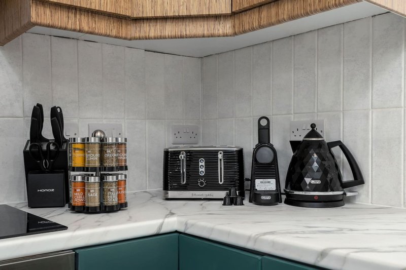 Modern kitchen counter with black appliances, storage containers, and white marble backsplash