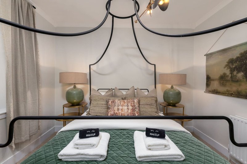 Bedroom with black metal bed frame, green bedding, white towels, and pendant lighting fixture