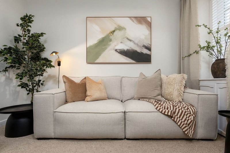 Modern living room with light gray sofa, cushions, throw blanket, artwork and potted plants