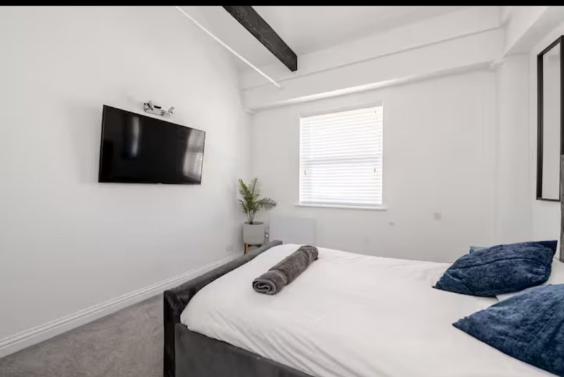 Modern bedroom with double bed, wall-mounted TV, window with blinds and decorative pillows