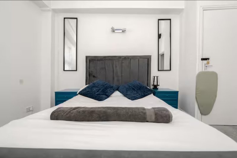 Modern bedroom with double bed, dark headboard, blue pillows and white bedding
