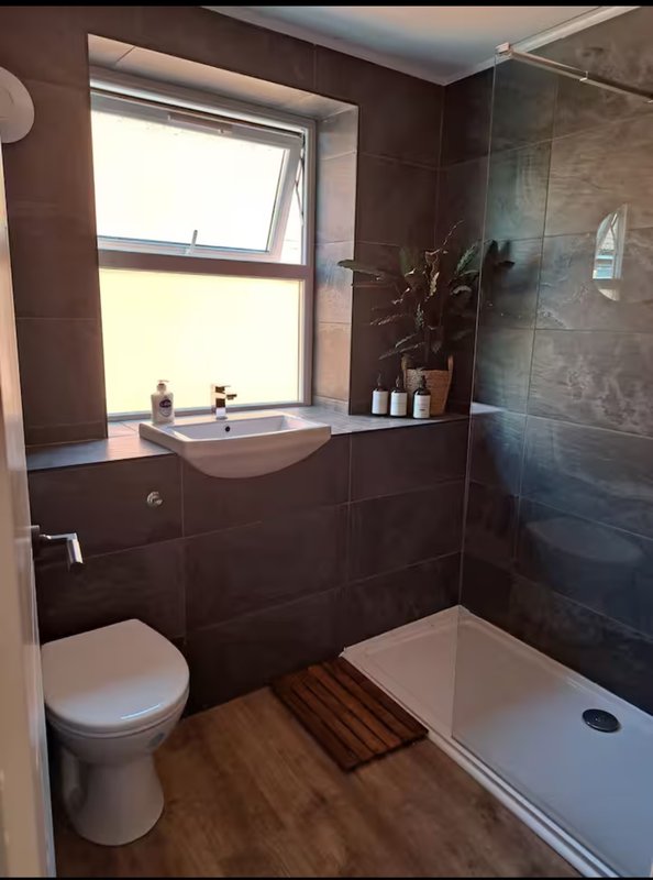 Modern bathroom with dark tile walls, sink, toilet, shower enclosure and window