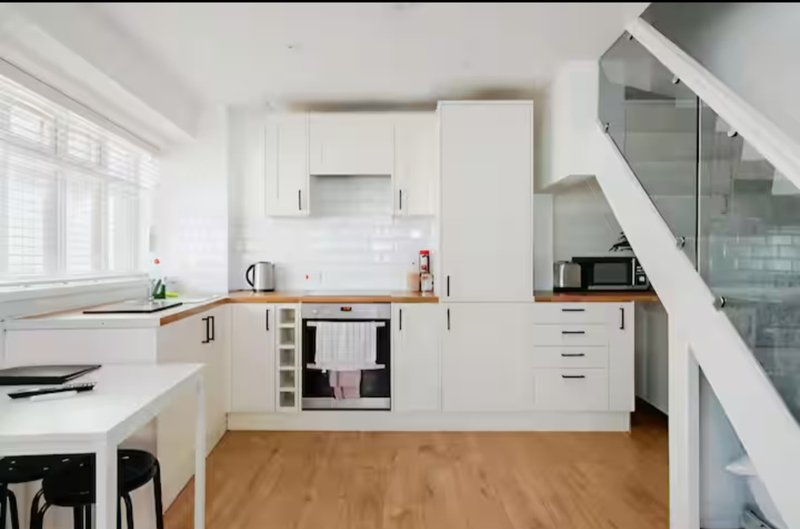 Modern white kitchen with wooden flooring, integrated appliances, and island seating area