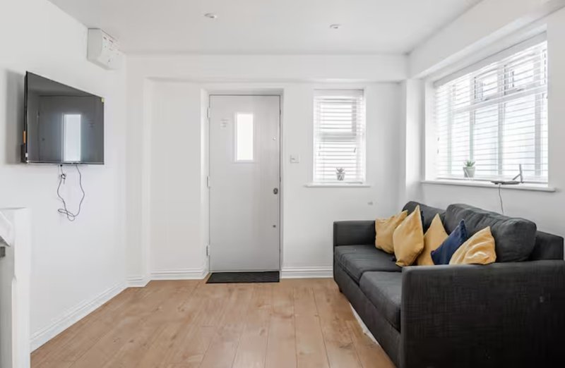 Bright living room with dark sofa, yellow cushions, wall-mounted TV, wooden flooring and shuttered windows