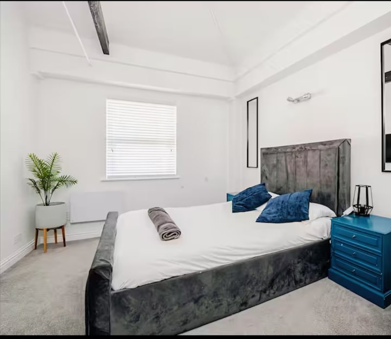 Modern bedroom with grey upholstered bed, blue bedside table, white bedding and blue cushions