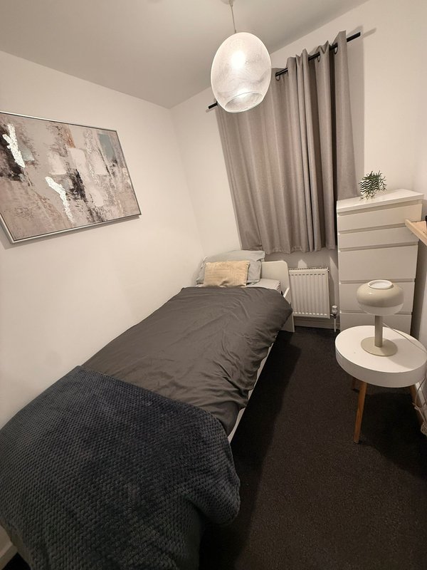 Compact bedroom with single bed, pendant light, white furniture and grey curtains