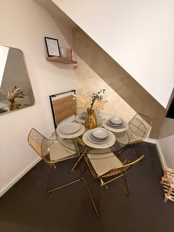 Dining nook with glass table, place settings, wire chairs and wall shelf