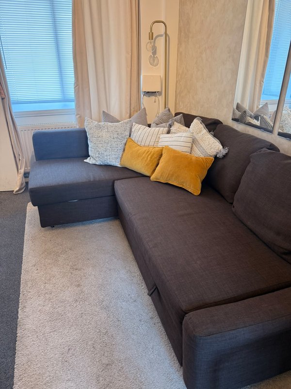 Living room with dark sectional sofa, yellow and striped cushions, windows with curtains
