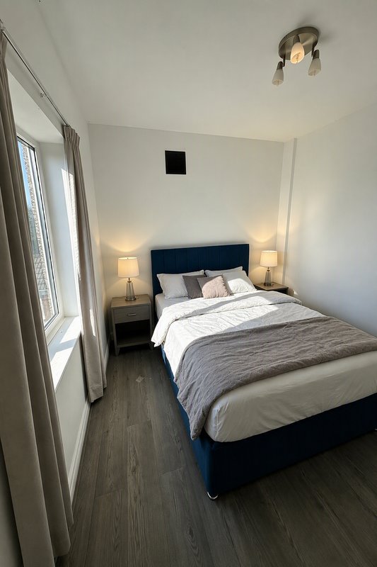 Modern bedroom with navy bed frame, white bedding, two bedside lamps and wooden floor