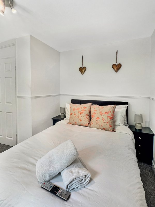 Bright bedroom with double bed, white bedding, decorative heart ornaments, and black nightstand