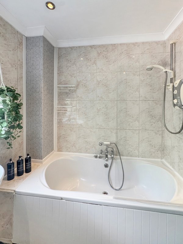 Modern bathroom with white bathtub, marble tile surround, and glass shower enclosure