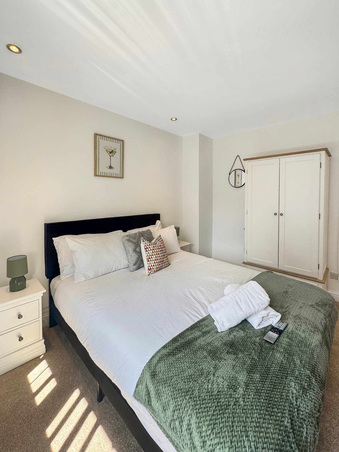 Bright bedroom with double bed, black headboard, white bedding, green throw, and mirrored wardrobe