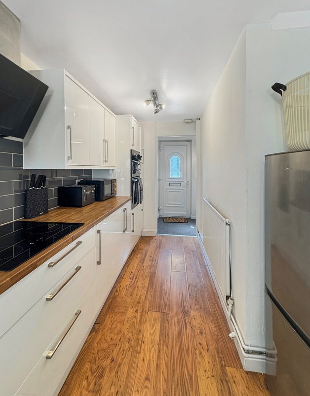 Modern galley kitchen with white cabinetry, wooden worktops, stainless steel appliances and wooden flooring