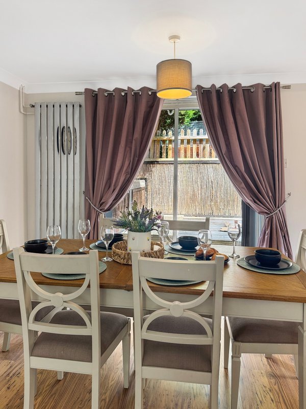 Dining room with white chairs, wooden table, pendant lamp, and purple curtains framing window