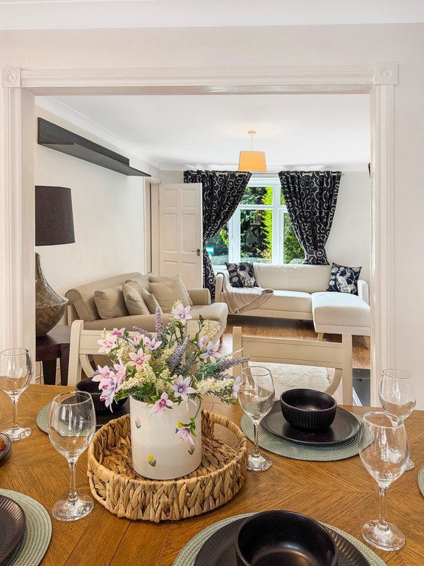 Dining table with flowers and place settings, open view to living room with sofa and window seating