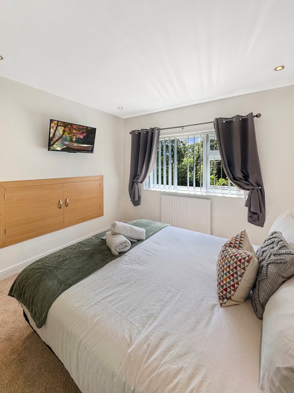 Bright bedroom with double bed, wooden headboard, patterned cushions and radiator below window