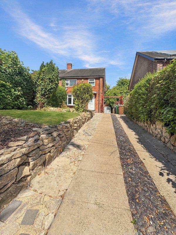 Red brick house with driveway, stone walls, and manicured green lawn