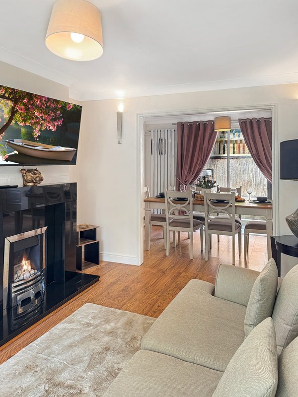 Living room with fireplace, sofa, dining area visible through doorway, wooden flooring