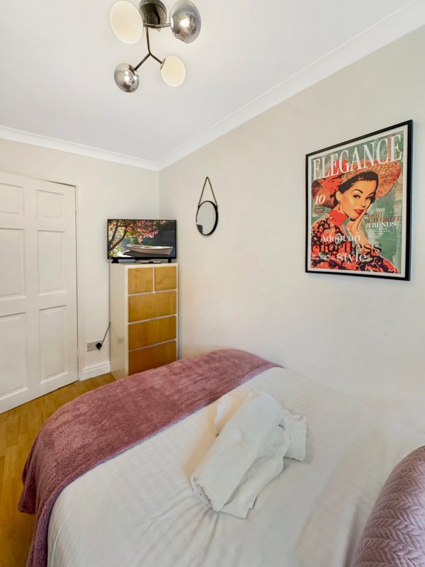 Bedroom with double bed, wooden dresser, wall art poster, and ceiling light fixture