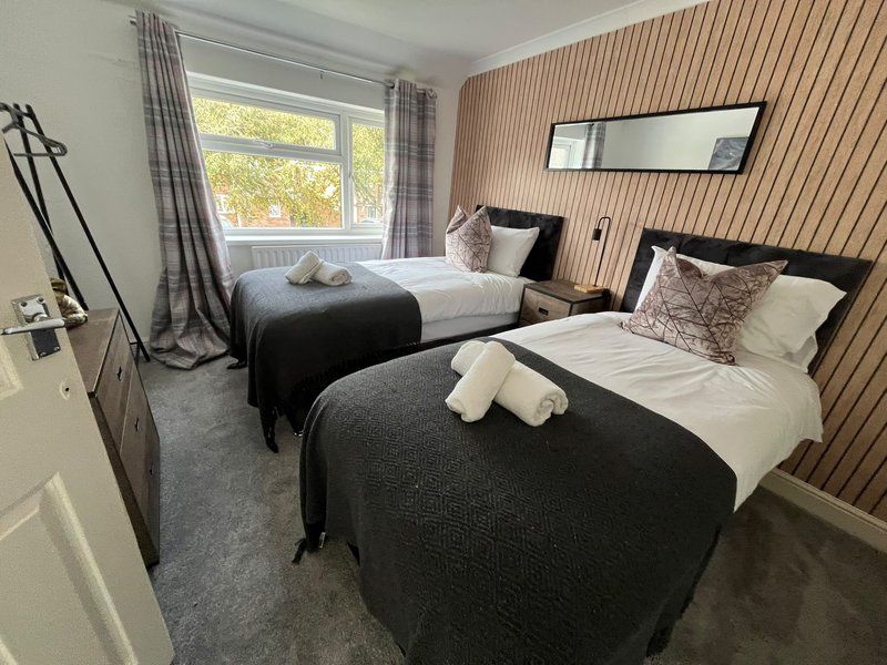 Twin bedroom with two black beds, corrugated accent wall, window with curtains and folded towels
