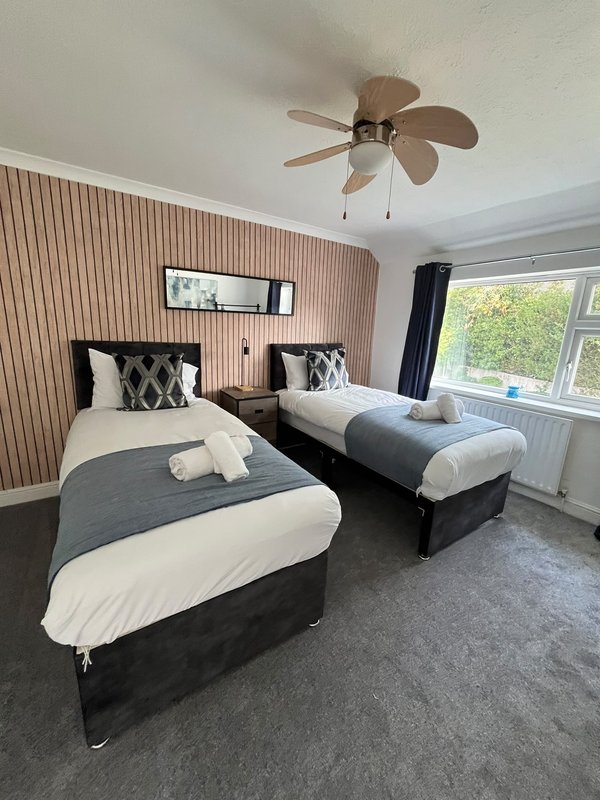 Twin bedroom with two single beds, ceiling fan, pink ribbed wallpaper and window view
