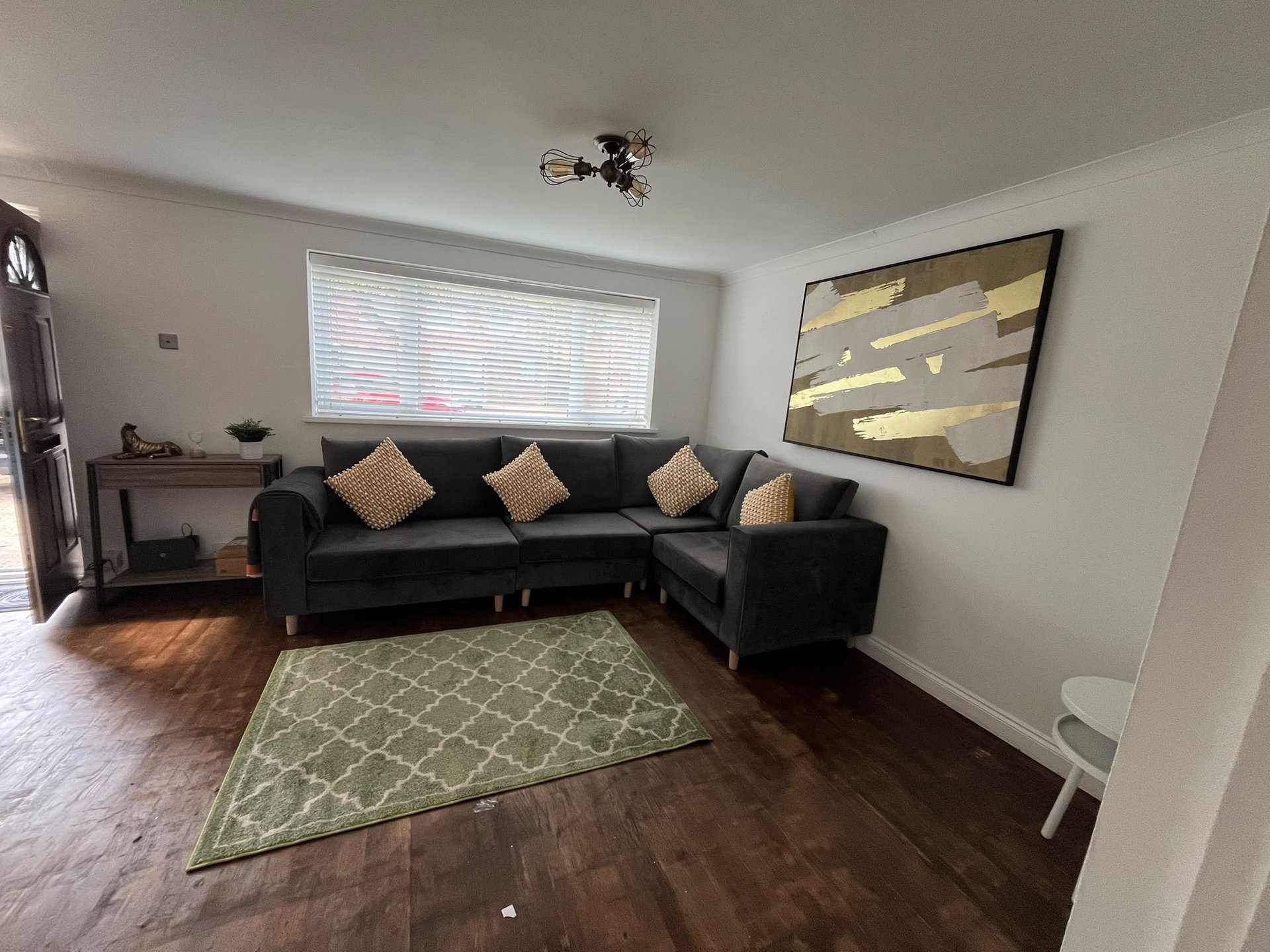 Living room with black corner sofa, geometric rug, wall art and window blinds