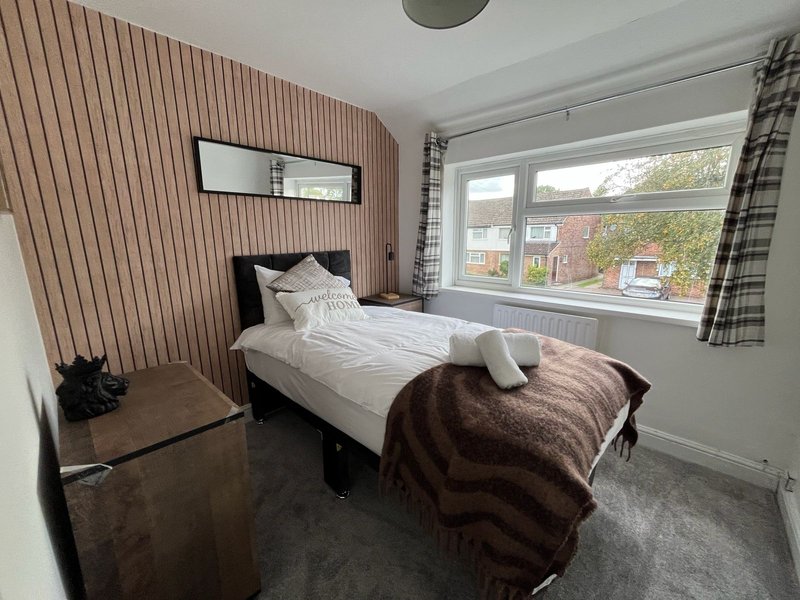 Bedroom with single bed, brown throw blanket, wooden chair, and large window overlooking garden