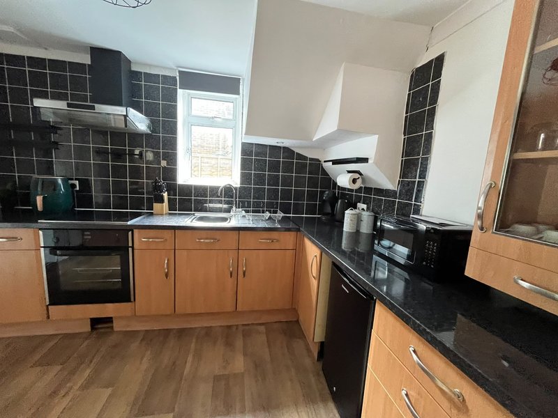 Kitchen with wooden cabinets, black countertops, black tile splashback and integrated appliances
