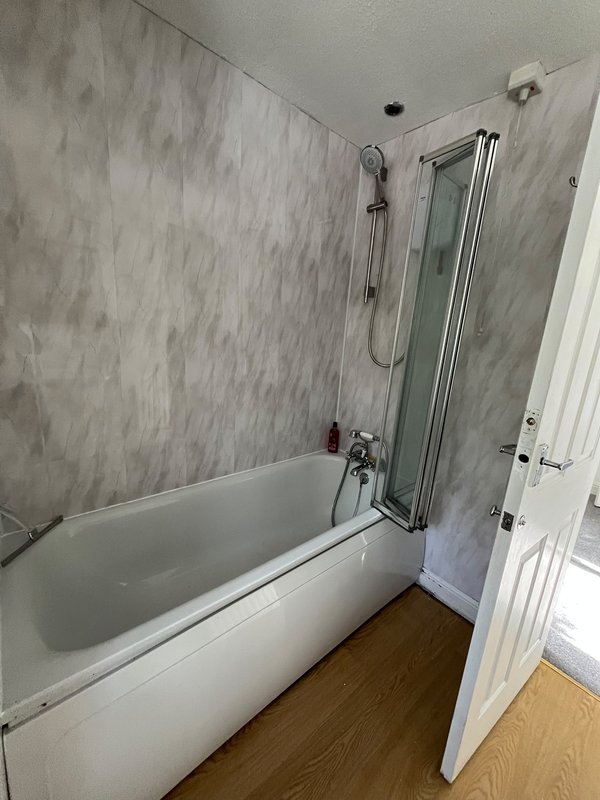 Bathroom with white bathtub, glass shower screen, grey tile walls and wooden flooring