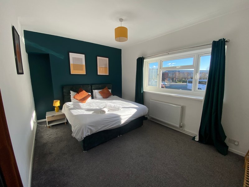 Bedroom with double bed, dark teal feature wall, orange accents, and large window with water view