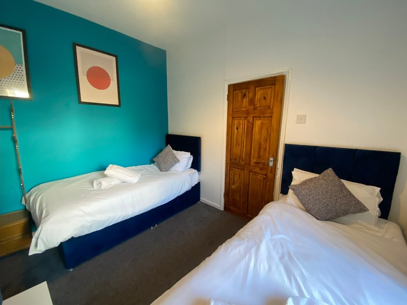 Shared bedroom with two single beds, turquoise accent wall, wooden door and minimal decor