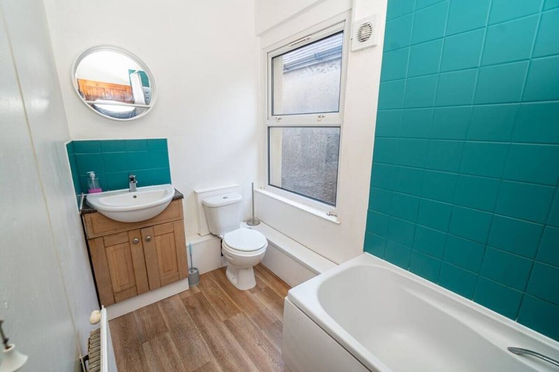 Modern bathroom with teal tile wall, white sink, toilet, bathtub and window