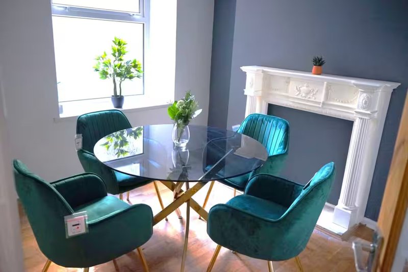 Modern dining room with round glass table, teal velvet chairs, fireplace and window