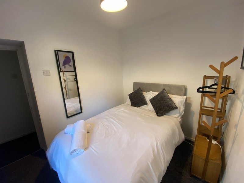 Bedroom with double bed, grey headboard, white bedding, wooden coat stand and framed mirror