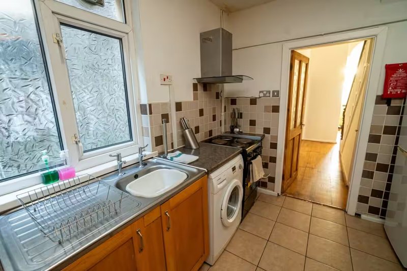 Kitchen with orange cabinets, cooker, washing machine, and tiled backsplash