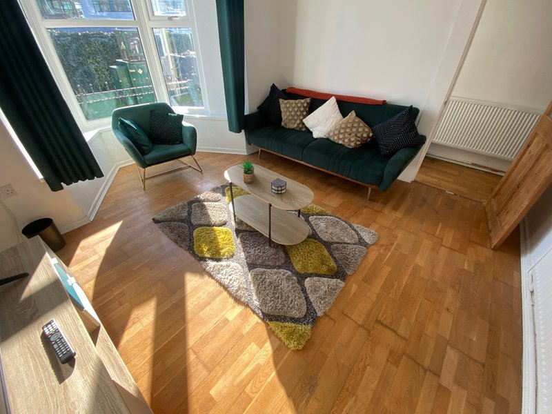 Bright living room with green sofa, armchair, wooden floor and large windows