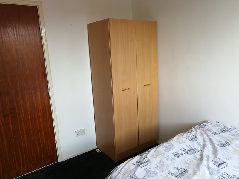 Bedroom with wooden wardrobe, single bed with patterned bedding, and brown door