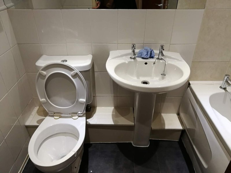 Bathroom with toilet, pedestal sink, and tiled walls with basic fixtures