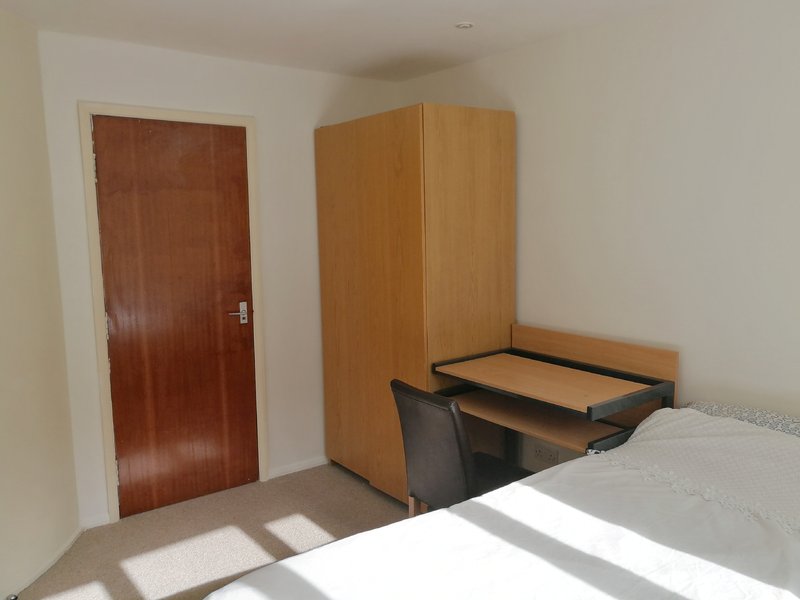Bedroom with single bed, wooden wardrobe, desk, and brown door
