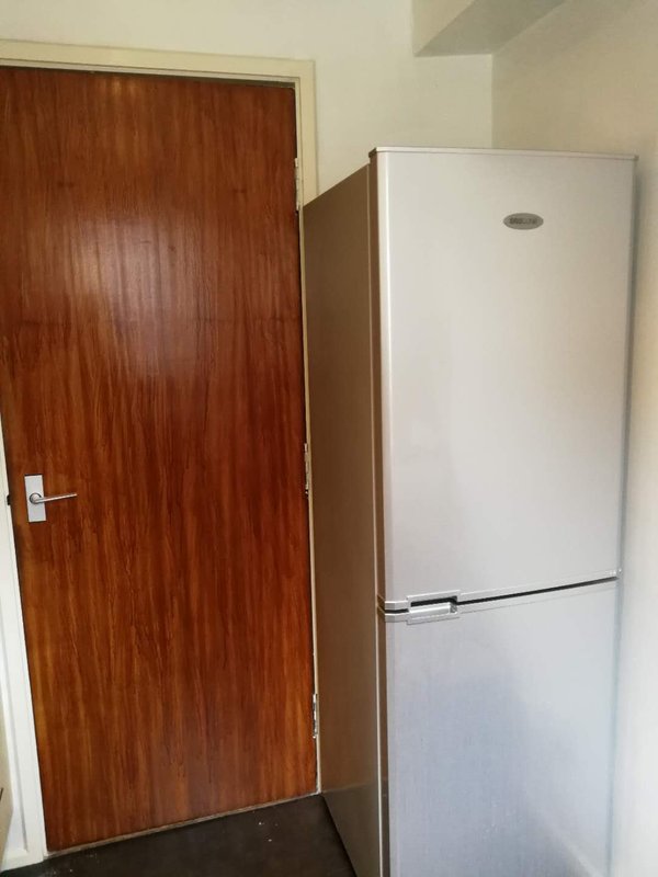 Kitchen area with wooden door, white refrigerator freezer, and dark flooring