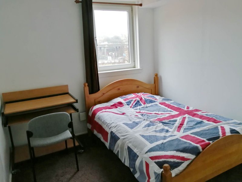 Bedroom with wooden bed frame, Union Jack duvet, chair, desk and window with city view