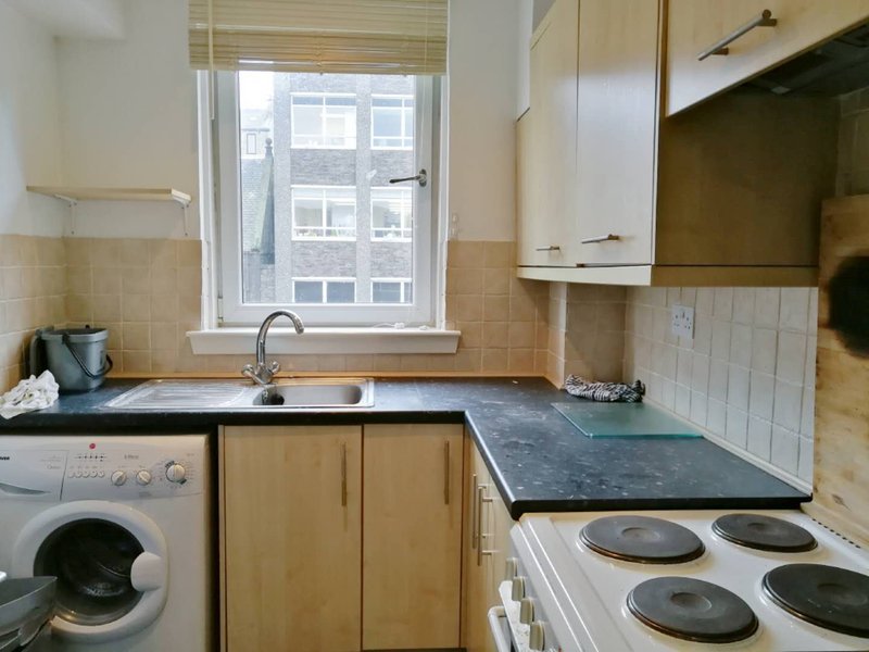 Small kitchen with wooden cabinets, sink, washing machine, electric cooker and window