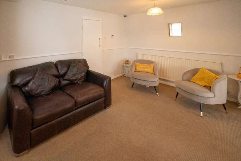 Spacious living room with brown leather sofa, beige armchair, side table and yellow cushions
