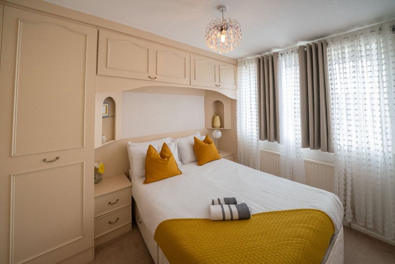 Modern bedroom with built-in wardrobe, double bed, yellow accents, pendant light, and sheer curtains