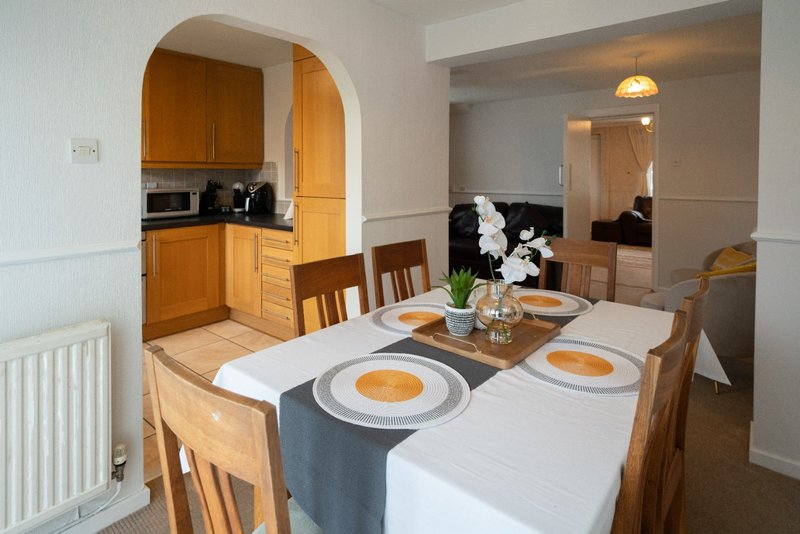 Open-plan dining and kitchen area with wooden table, chairs, and arched doorway to kitchen