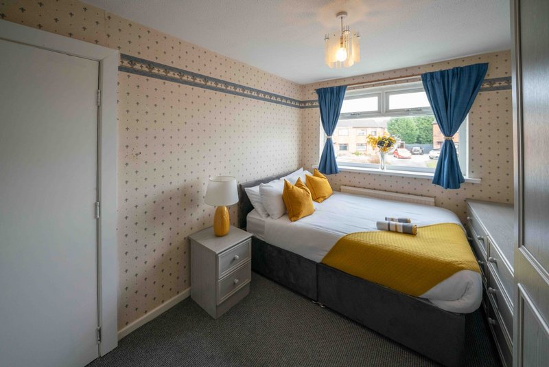 Bright bedroom with single bed, yellow bedding, patterned wallpaper and blue curtains