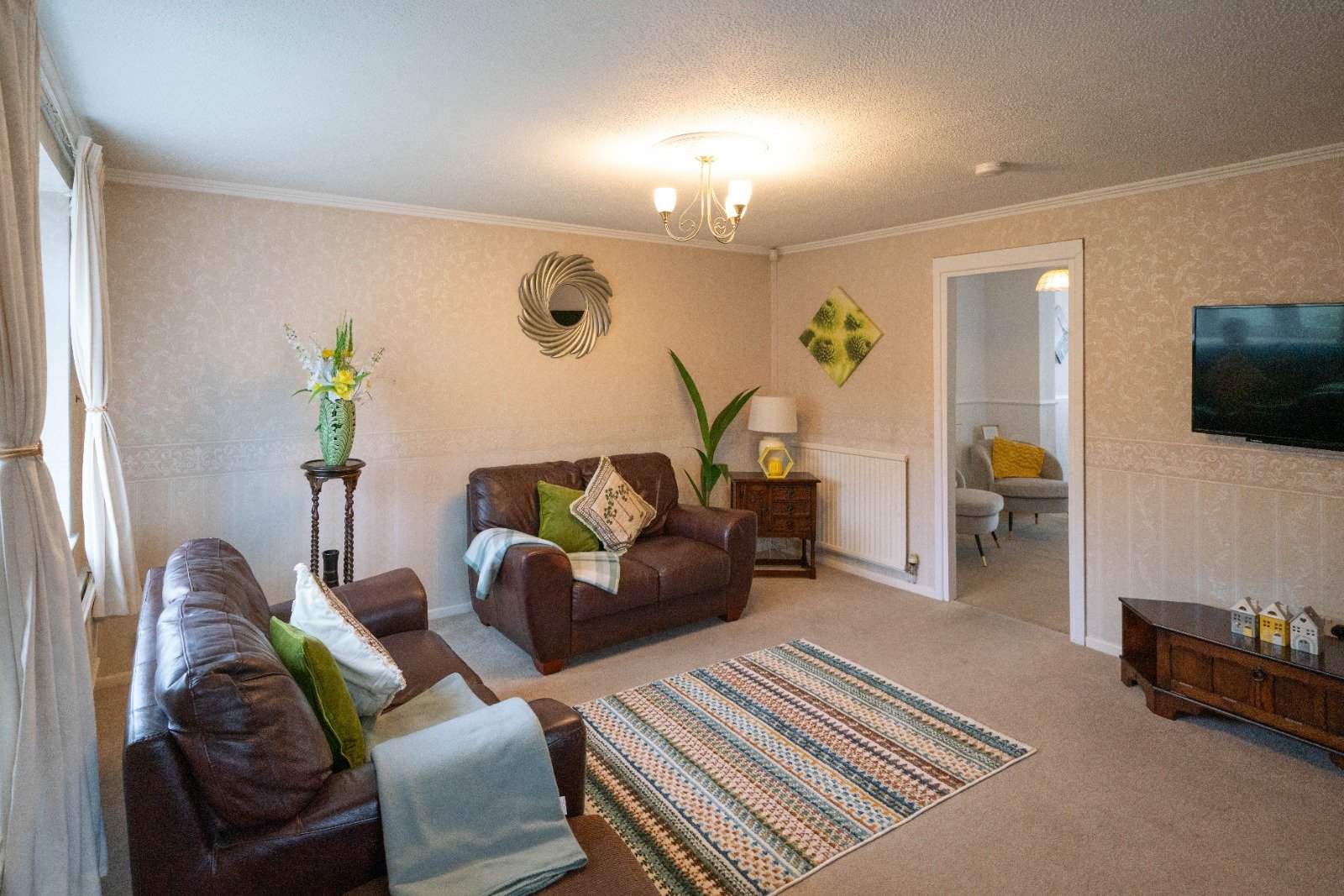 Spacious living room with brown leather sofas, striped rug, wall-mounted TV, and access to adjoining rooms