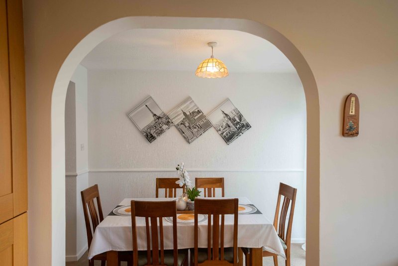 Dining room with wooden table, four chairs, white tablecloth, and framed black and white photographs on wall